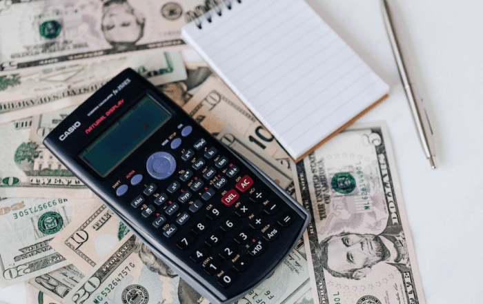 A calculator and a notepad placed on dollar bills